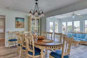 A dining area with a wooden table and chairs, a chandelier, and a view of the outdoors through large windows.