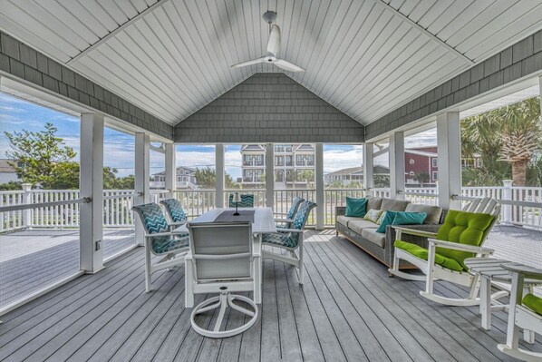 A covered outdoor deck with a table and chairs, a sofa, and rocking chairs.