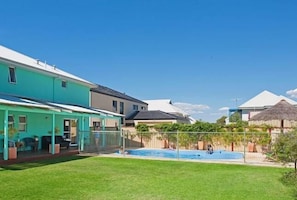 A residential area with a swimming pool, houses with white roofs, and a clear blue sky.