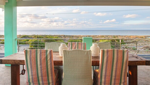 Een tafel met gestreepte stoelen en decoratieve vazen, met uitzicht op een kustlandschap en de zee in de verte.