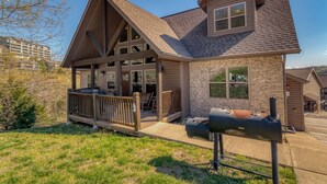 A two-story house with a stone facade, a wooden deck, and a barbecue grill in the front yard. - Boat Slip Included, Lake Views, Close to SDC! (Branson)