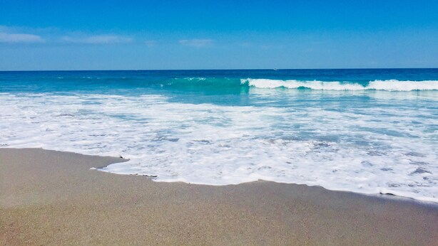Une plage où les vagues se brisent près du rivage, sous un ciel dégagé.