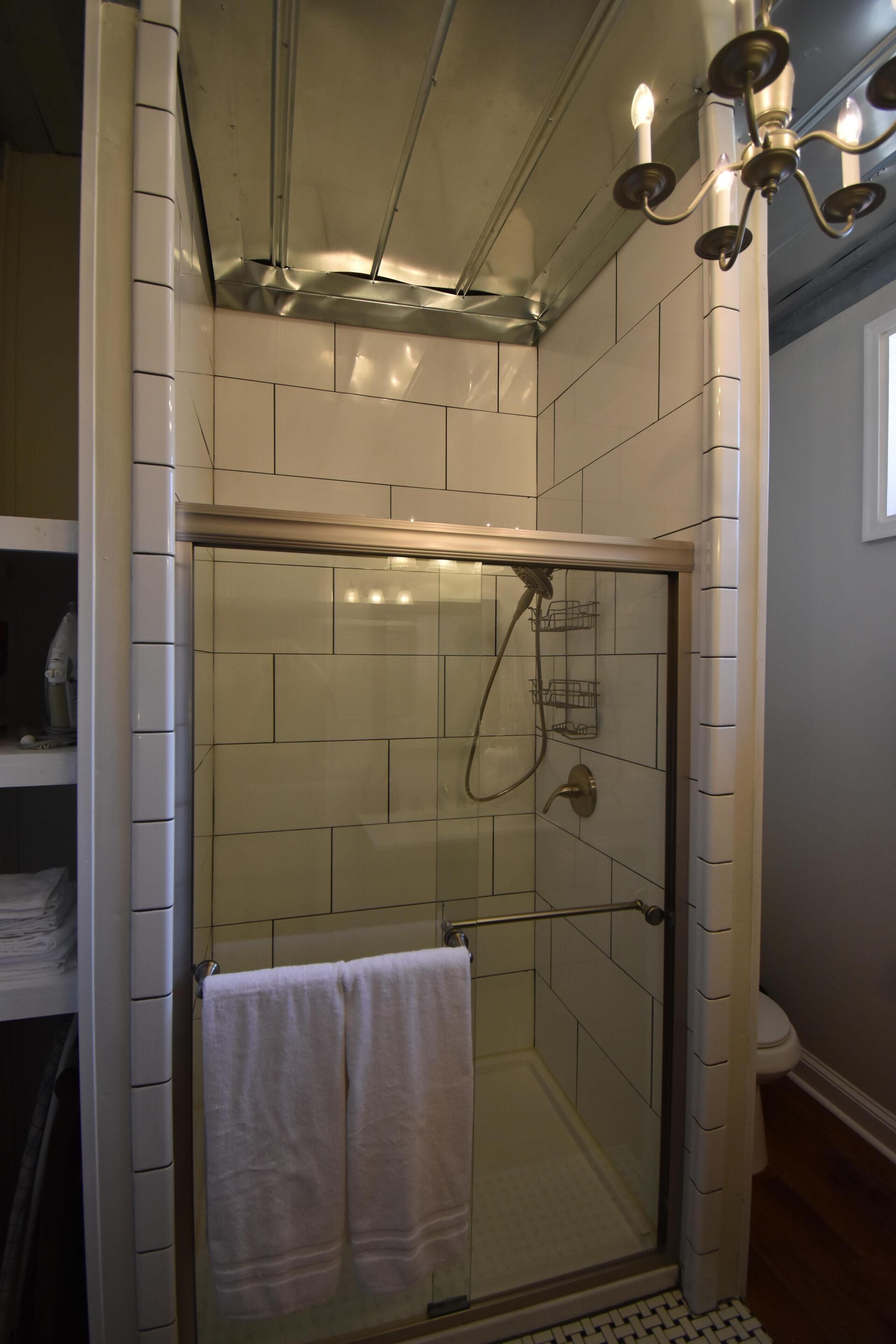 A shower with a glass door, a towel rack with two towels, and a light fixture above.