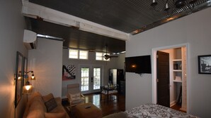 A spacious living area with a sofa, a coffee table, and a patterned bedspread. There is a dining table with chairs, a kitchen area, and a door leading to another room. - The Cottage in the Historic South Main Arts District, Walk Everywhere Downtown (Memphis)