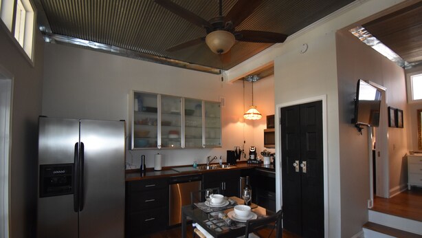 A modern kitchen with a stainless steel refrigerator, wooden cabinets, and a dining area with a table set for two. - The Cottage in the Historic South Main Arts District, Walk Everywhere Downtown (Memphis)