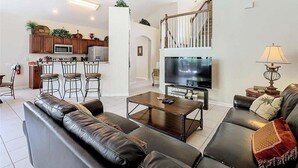 Een moderne woonkamer met een zithoek, een salontafel, een televisie en een keukenhoek met barstoelen.