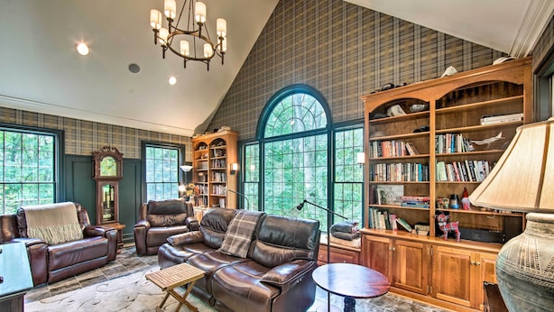 Un salon spacieux, doté de canapés en cuir, d’une bibliothèque en bois et d’une grande fenêtre donnant sur la verdure.