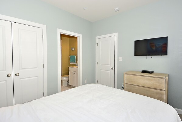 Un dormitorio con cama, cómoda, televisor y dos puertas que dan a un baño.