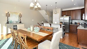 Una cocina moderna con armarios de madera, un refrigerador de acero inoxidable y un comedor con mesa y sillas de madera.