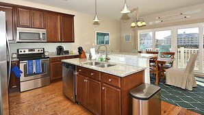 Una cocina con armarios de madera, electrodomésticos de acero inoxidable, encimera de granito y vistas a la ciudad a través de amplios ventanales.