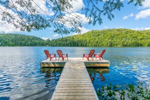 A wooden dock with red chairs extending into a calm lake, surrounded by lush greenery and a clear sky. - Locations du Sommet - Grand Lodge (St-Adolphe-d'Howard)