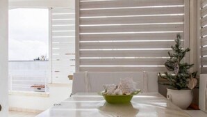 Un coin repas avec une table dressée pour deux personnes, un saladier vert contenant des aliments, des chaises blanches et une plante en pot.