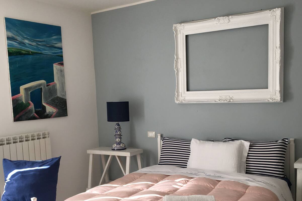 A bedroom with a bed, a nightstand, a lamp, a framed picture, and a chair.