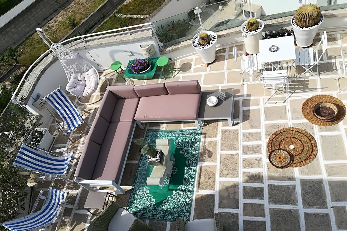 An outdoor patio with a sectional sofa, striped lounge chairs, a small pool, and potted plants.