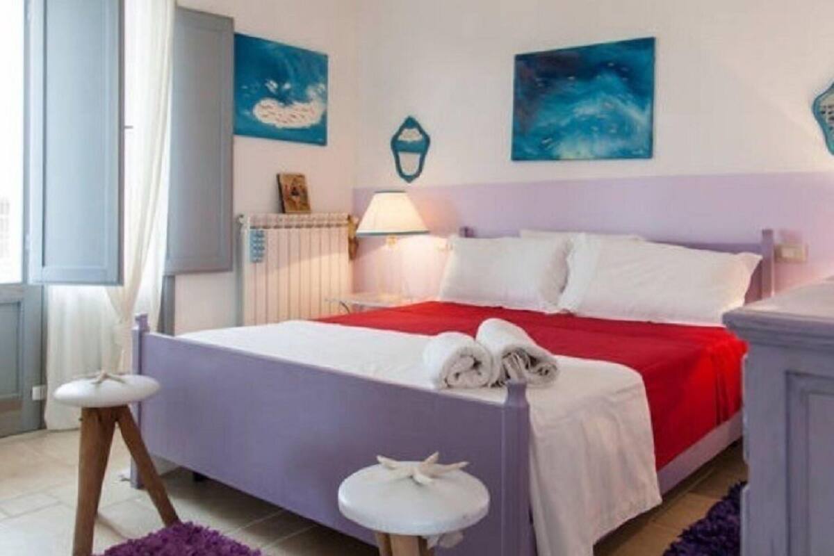 A bedroom with a bed, a bedside table, a lamp, and artwork on the walls.