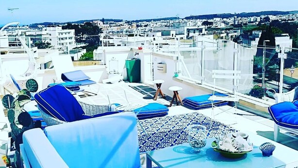Une terrasse sur le toit, agrémentée de meubles bleus et blancs, d’une table en verre et offrant une vue sur le paysage urbain.