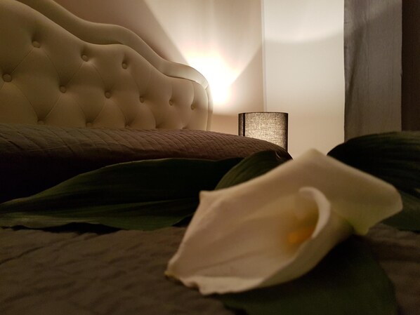 A bed with a tufted headboard, a bedside lamp, and a white calla lily on the bed.