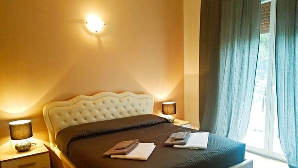 Una camera da letto con un letto grande, due comodini con lampade, una finestra con tende e un punto luce a parete.