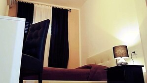 Un ambiente compatto con un letto, una sedia, un tavolino e una lampada.