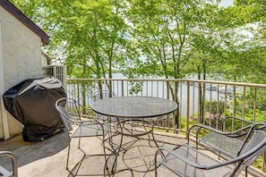 Une terrasse couverte avec une table ronde et des chaises, donnant sur un plan d’eau et des arbres.