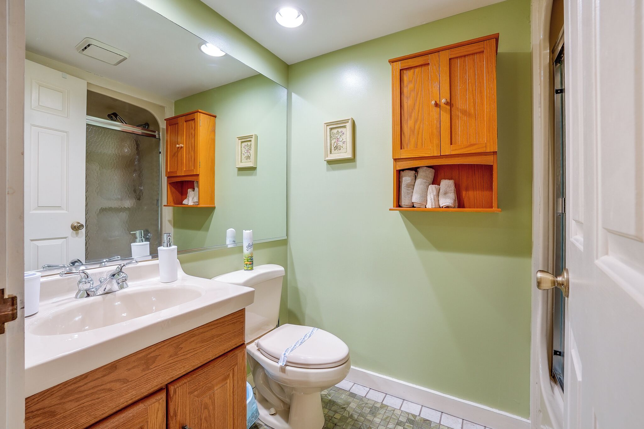 Un baño con lavamanos blanco, armarios de madera, un inodoro y un espejo.