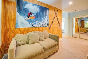 Een kamer met een houten wand, een groot schilderij van een skiër, en ski's die tegen de muur staan.