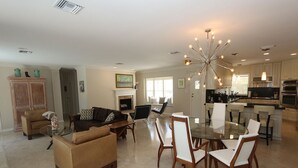 A spacious living room with a glass-top dining table surrounded by chairs, a fireplace, and a kitchen area with modern appliances. - Lido Key Home w Pool Near Beach & Shops: Rondy Home by RVA (Sarasota)