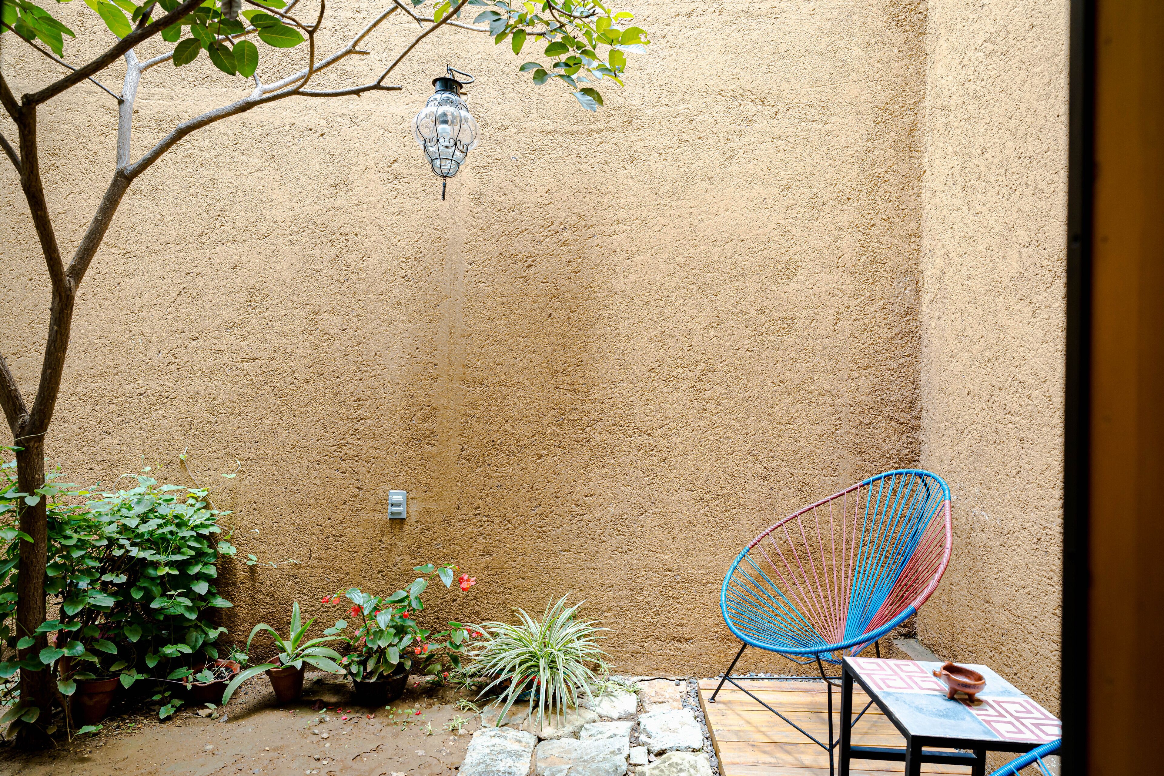 A patio with a blue chair, potted plants, a lantern, and a table.