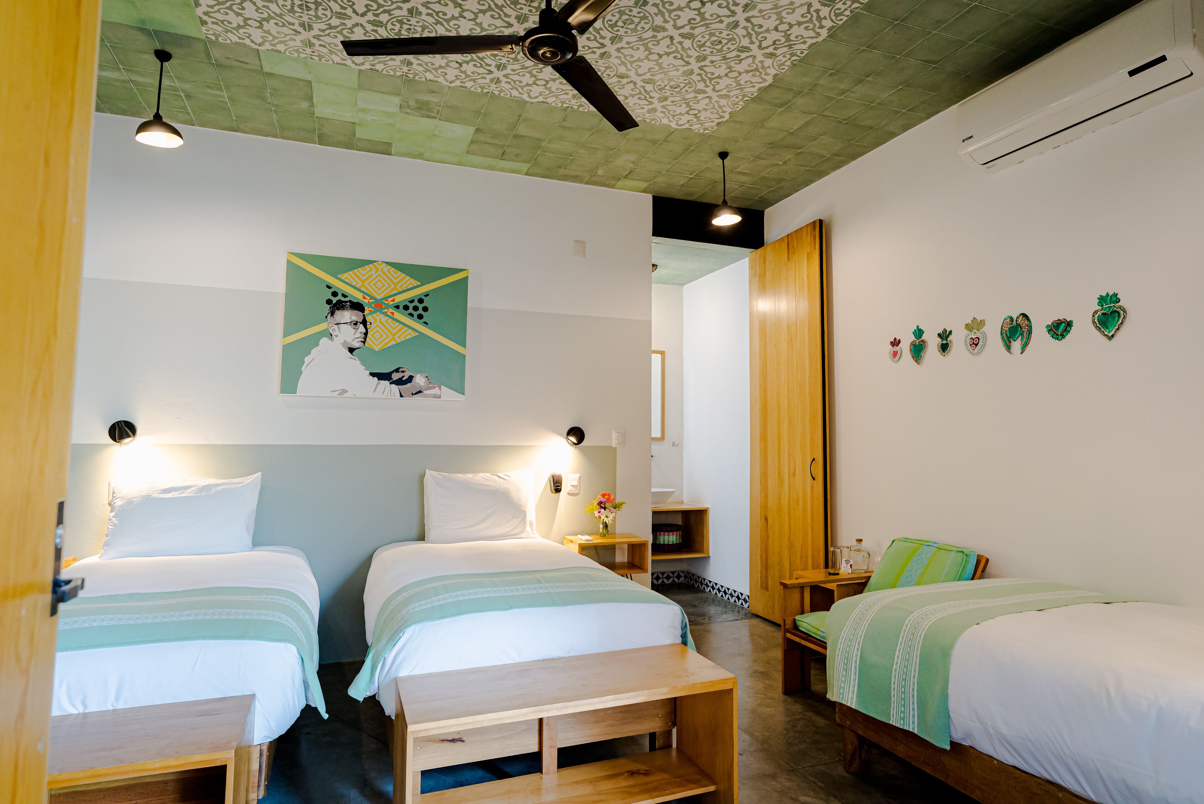 A hotel room with two beds, a ceiling fan, a decorative wall piece, and a small table.