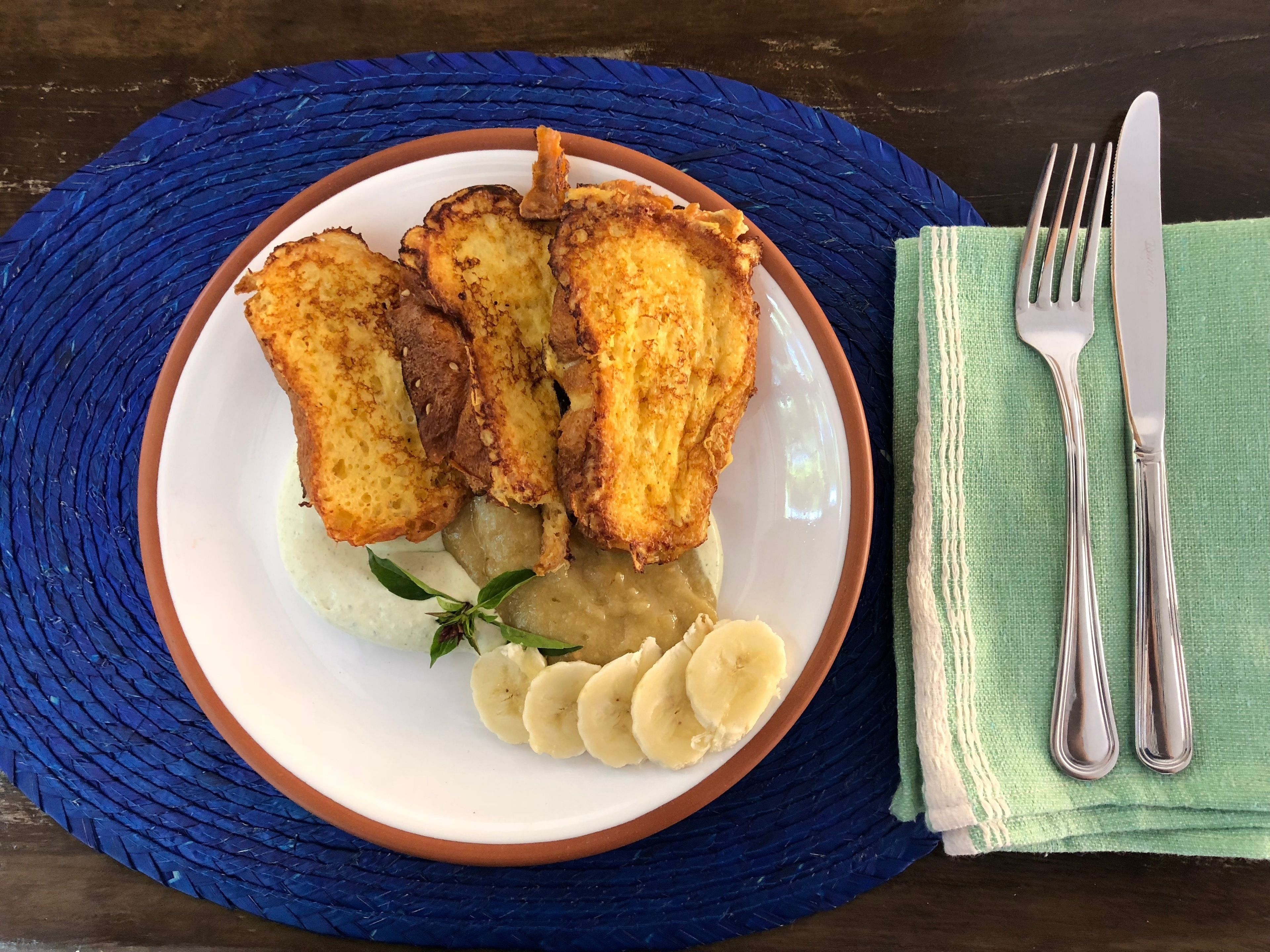 Un plato con pan tostado, rodajas de plátano y un pequeño adorno sobre un camino de mesa tejido azul.