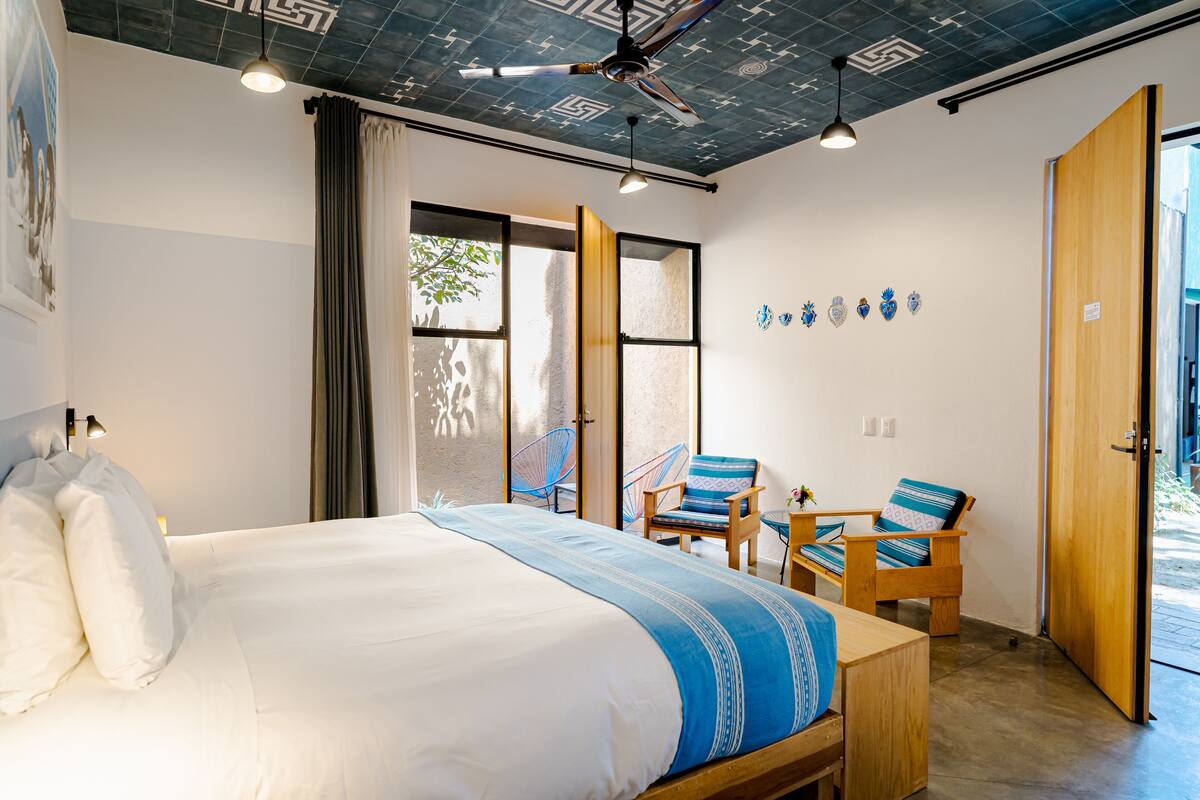 A bedroom with a bed, two chairs, a wooden table, and a ceiling fan.