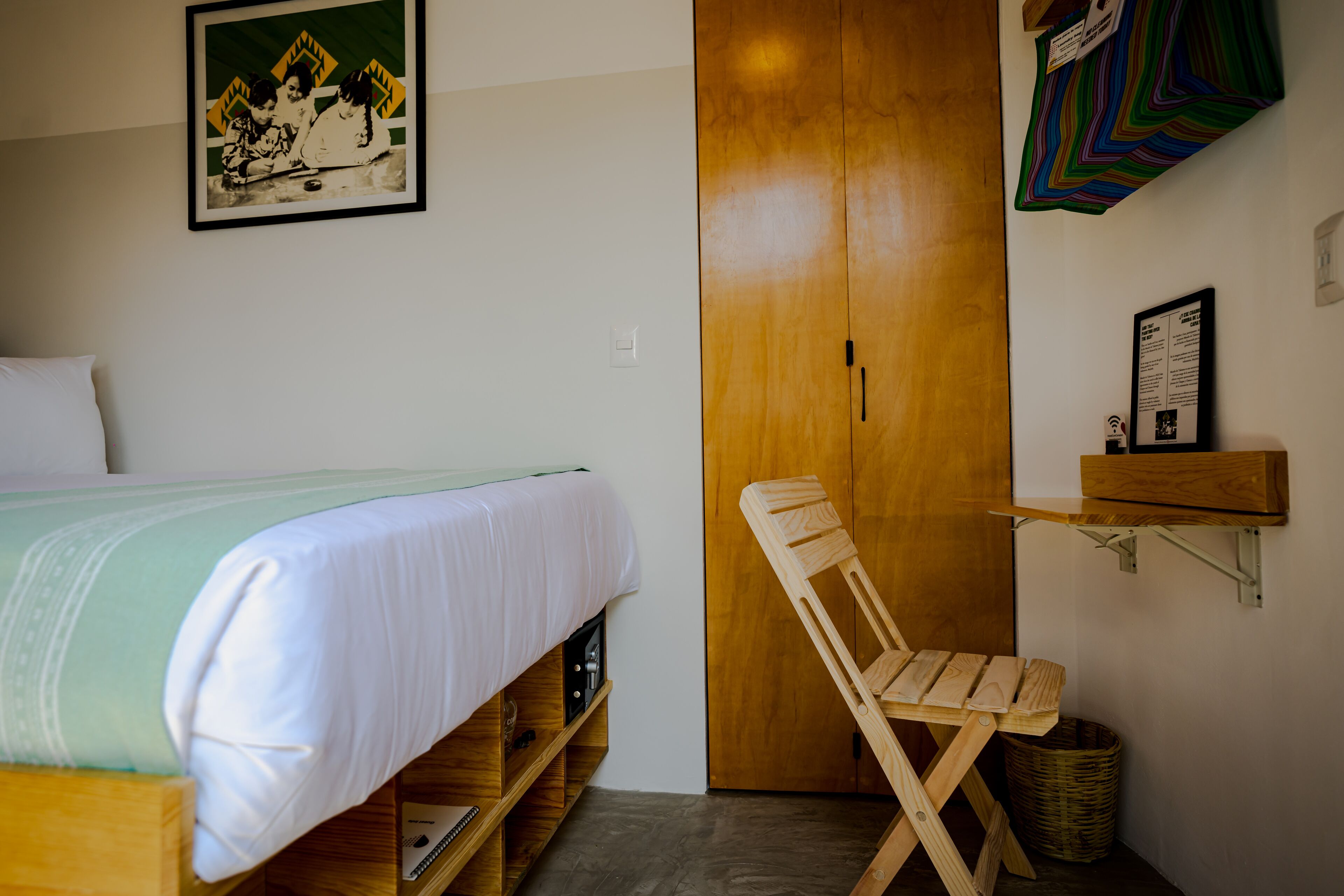 A bedroom with a bed, wooden wardrobe, a chair, and a shelf with a framed picture.