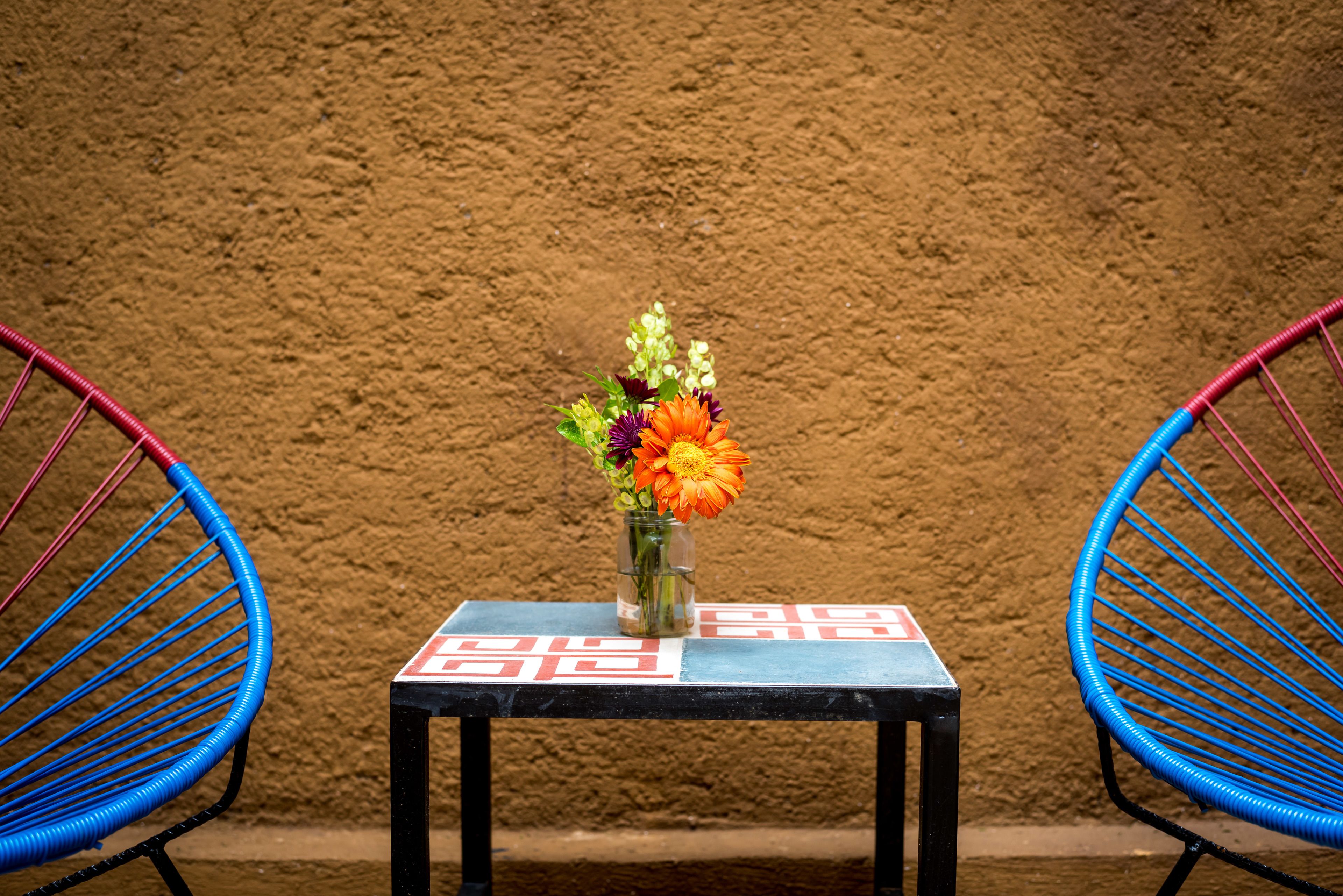 A small table with a vase of flowers and two blue chairs against a textured wall.