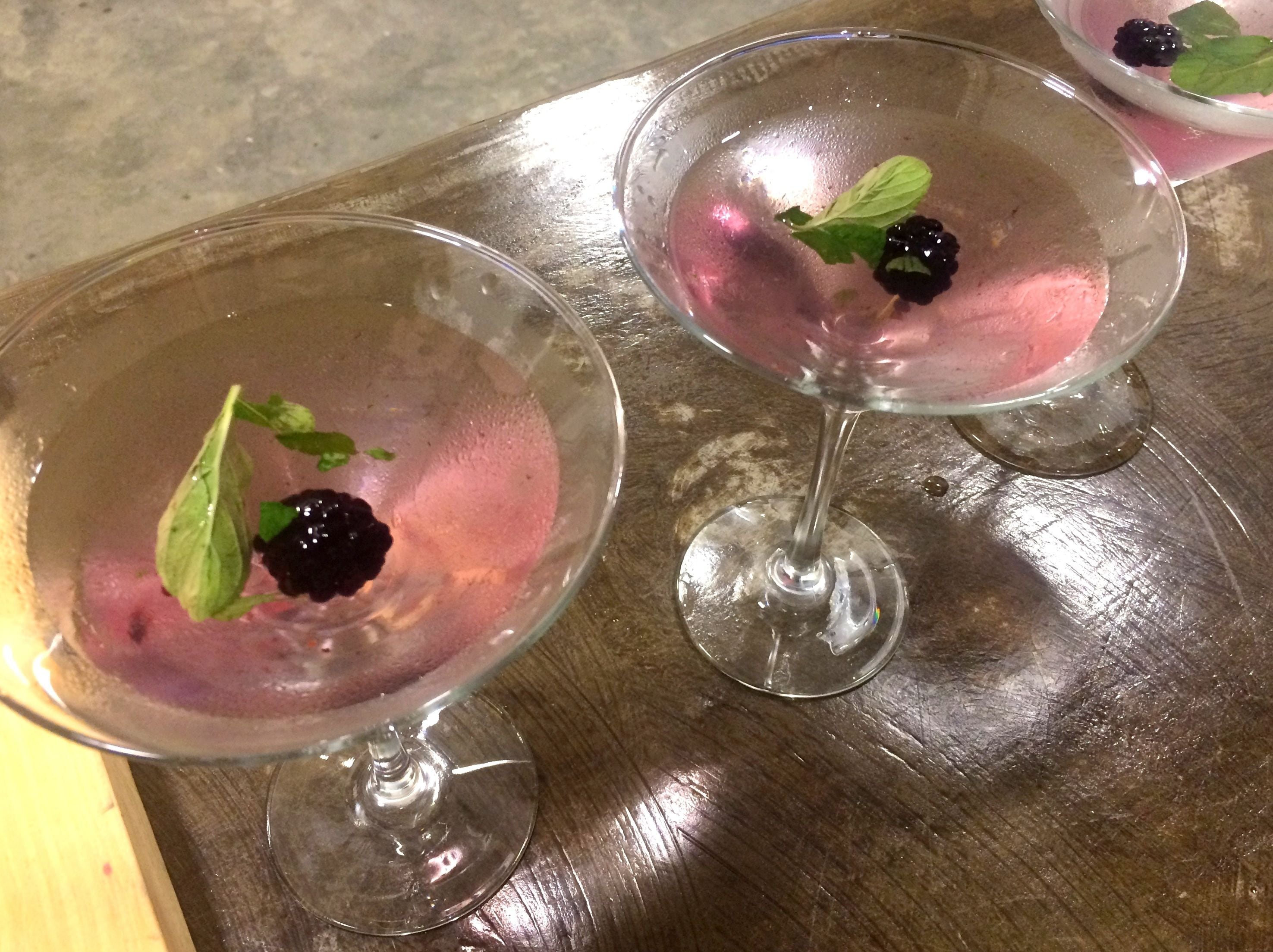Two glasses of pink beverage with blackberries and mint leaves on a wooden surface.