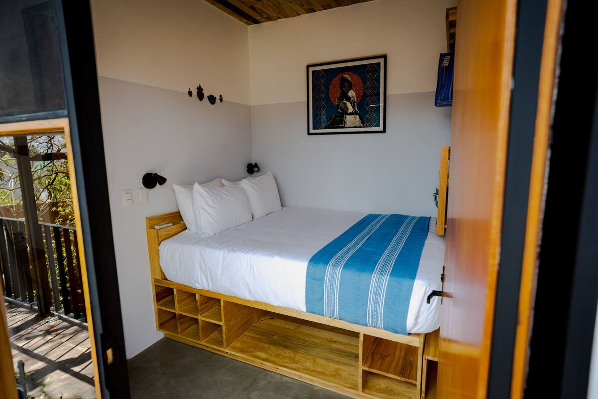 A single bed with a wooden frame, white bedding, and a blue and white striped blanket. There is a framed picture on the wall above the bed.