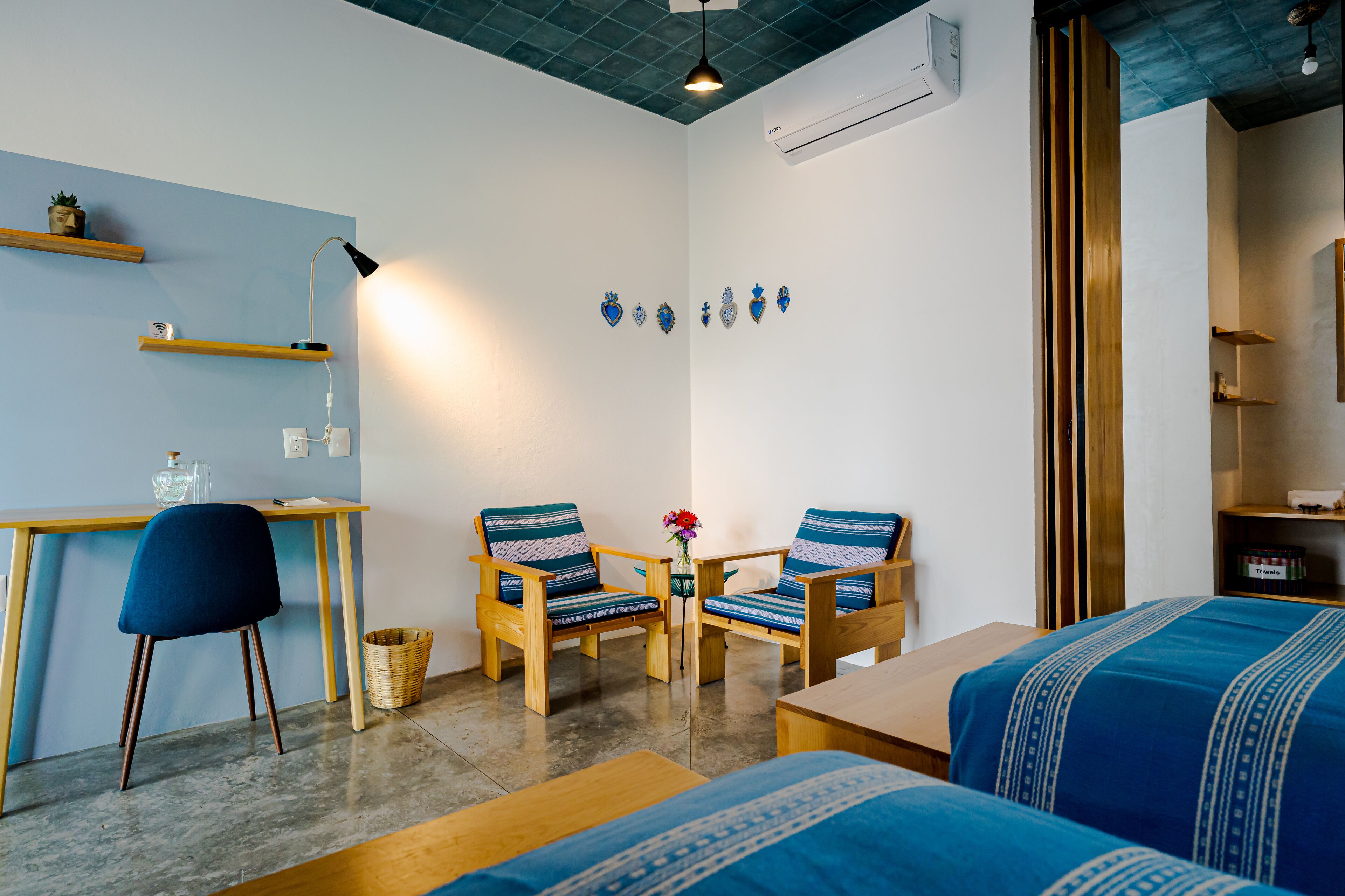 A compact room with a desk, two chairs, a small table, and two beds.