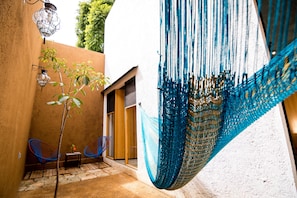 Relax and socialize in this serene outdoor seating area, featuring a table and two chairs under a hammock, surrounded by a tranquil garden.