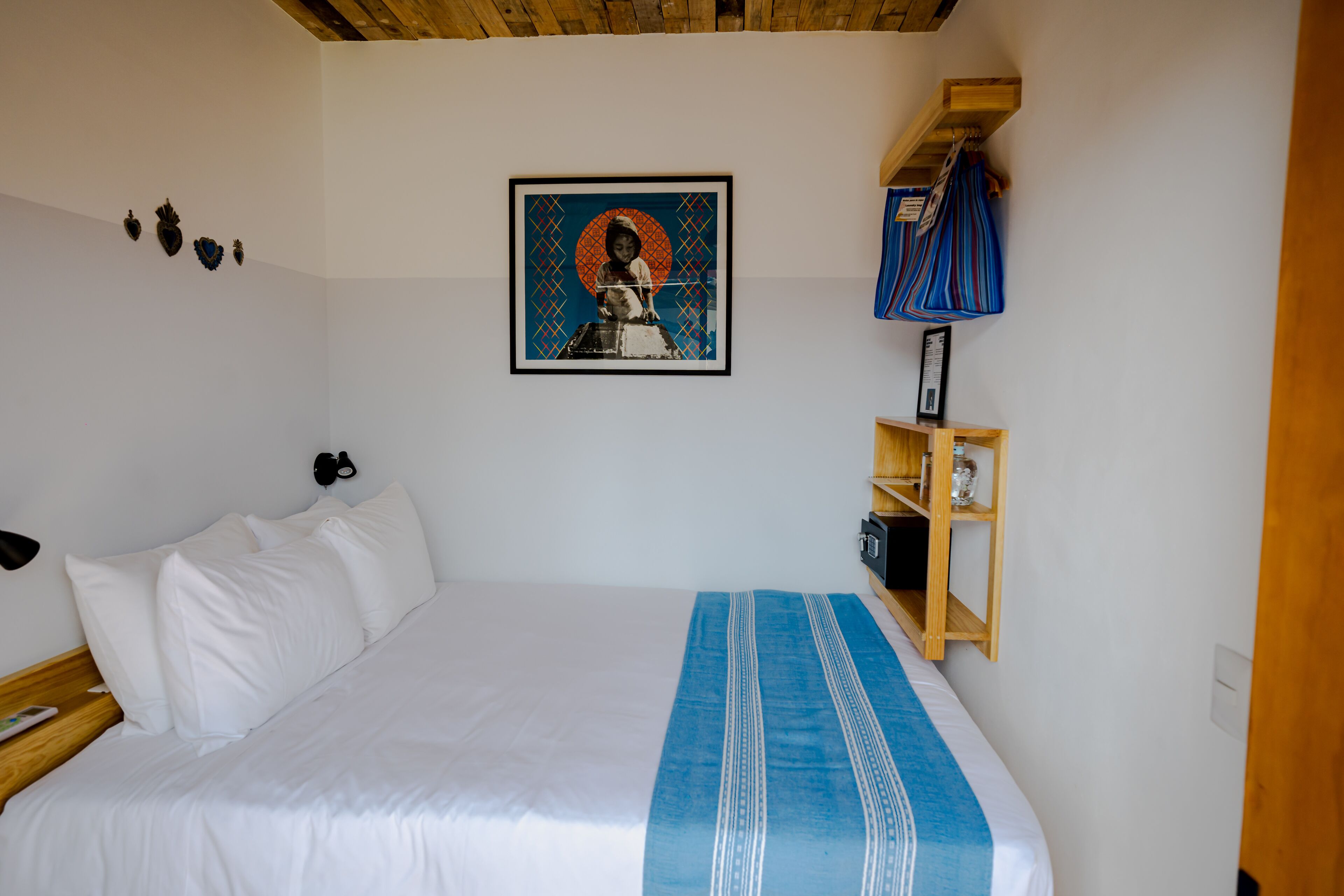 A neatly made bed with white linens and a blue accent, a wall-mounted shelf with a framed picture, and a wooden headboard.