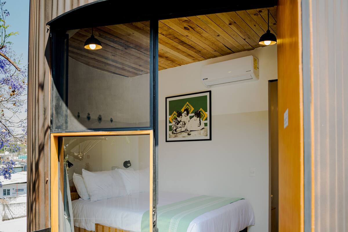 A compact, modern room with a bed, wooden shelves, and a glass door leading outside.