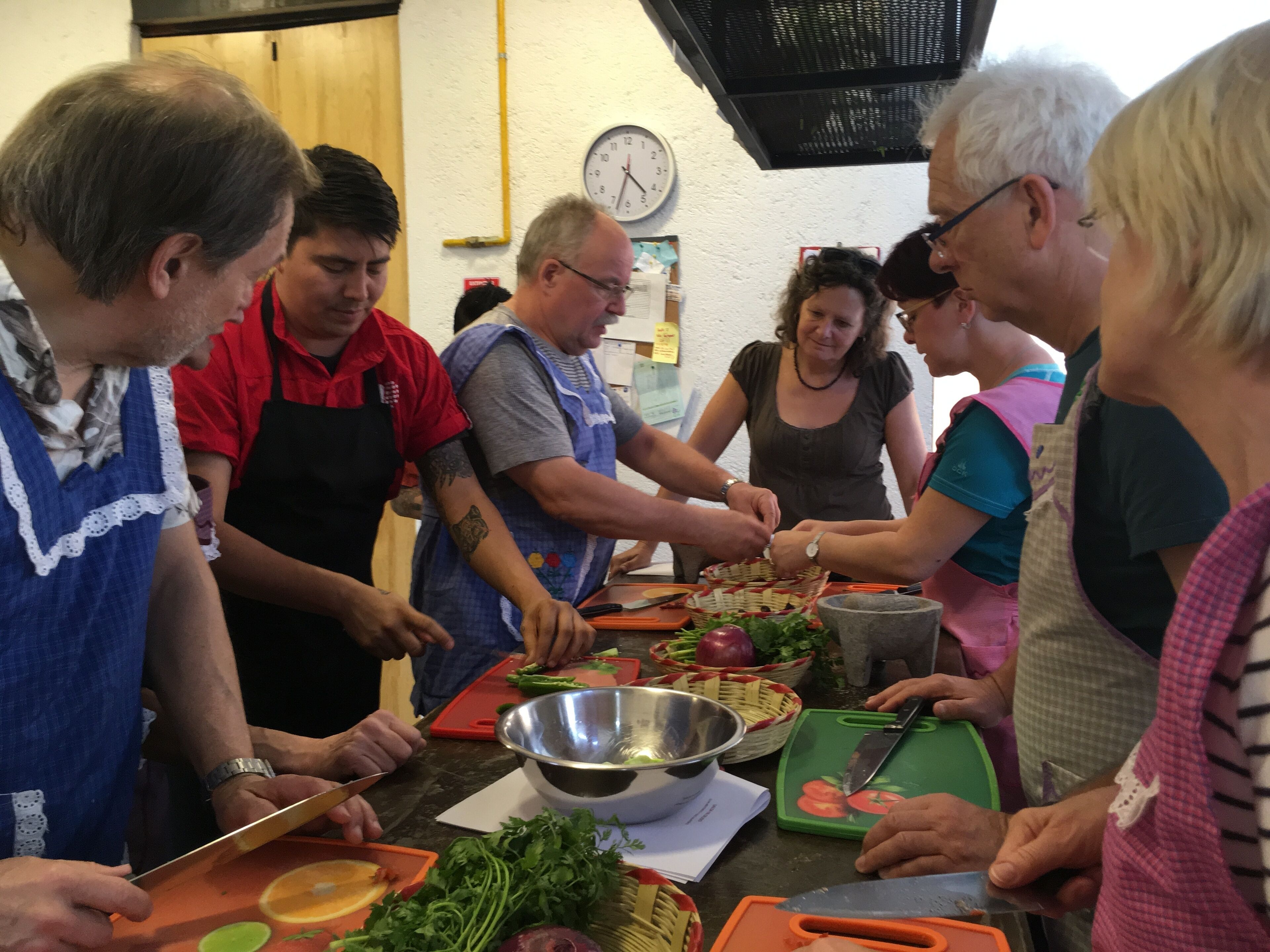Un groupe de personnes prépare des aliments dans une cuisine où l’on peut voir une horloge au mur.