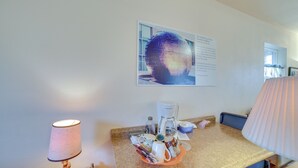 Hotelkamer met koffiezetapparaat, een lamp, een dienblad met bekers en een zakdoosje, en een poster aan de muur.