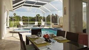 A covered outdoor dining area with a pool, chairs, and a table set for two.