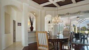 A dining area with a chandelier, wooden chairs, and a glass partition.