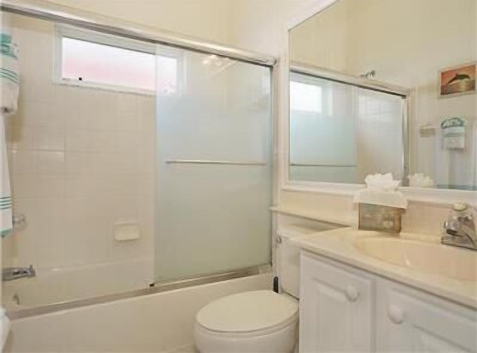 A bathroom with a glass-enclosed shower, a toilet, and a sink with a mirror above it.