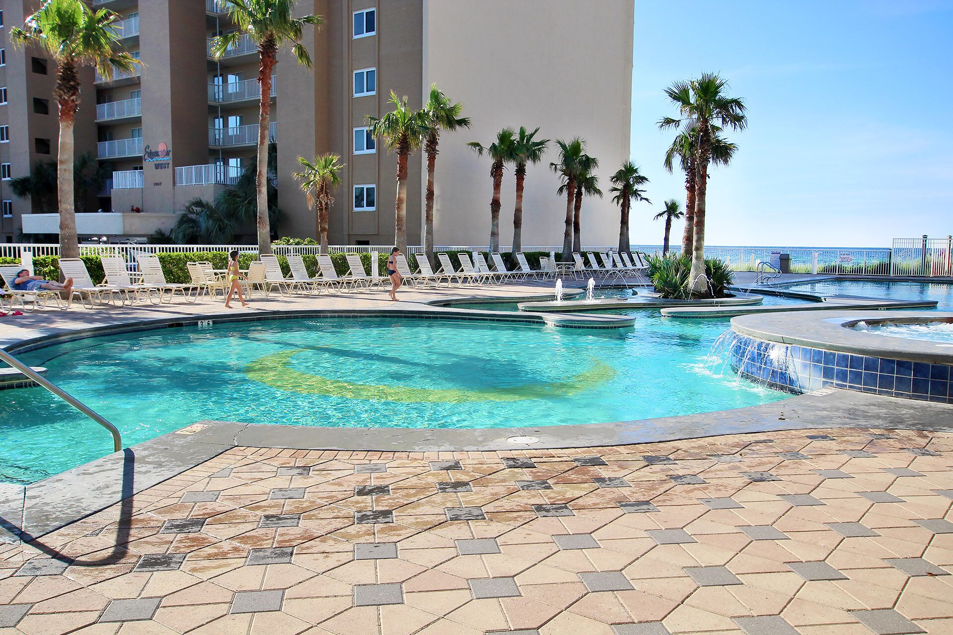 A swimming pool area with multiple pools, palm trees, and lounge chairs.