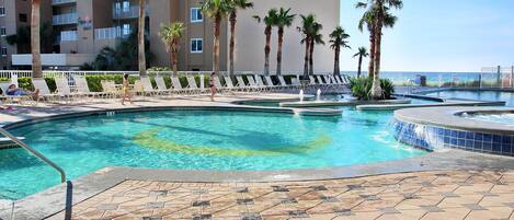 A swimming pool area with multiple pools, palm trees, and lounge chairs.