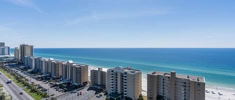 A coastal hotel with multiple high-rise buildings, a parking lot, and a beach view.