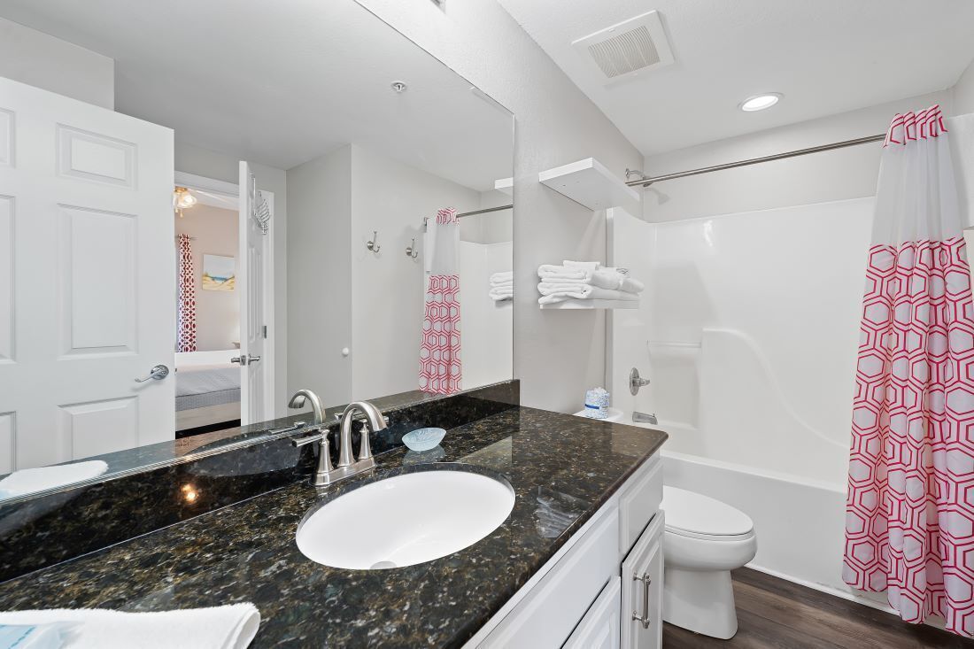 Un baño moderno con lavamanos de granito, inodoro blanco y ducha con cortina de patrón geométrico.
