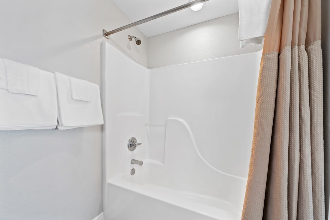 Un bagno moderno con box doccia in vetro, un portasciugamani con asciugamani bianchi e una tenda beige.