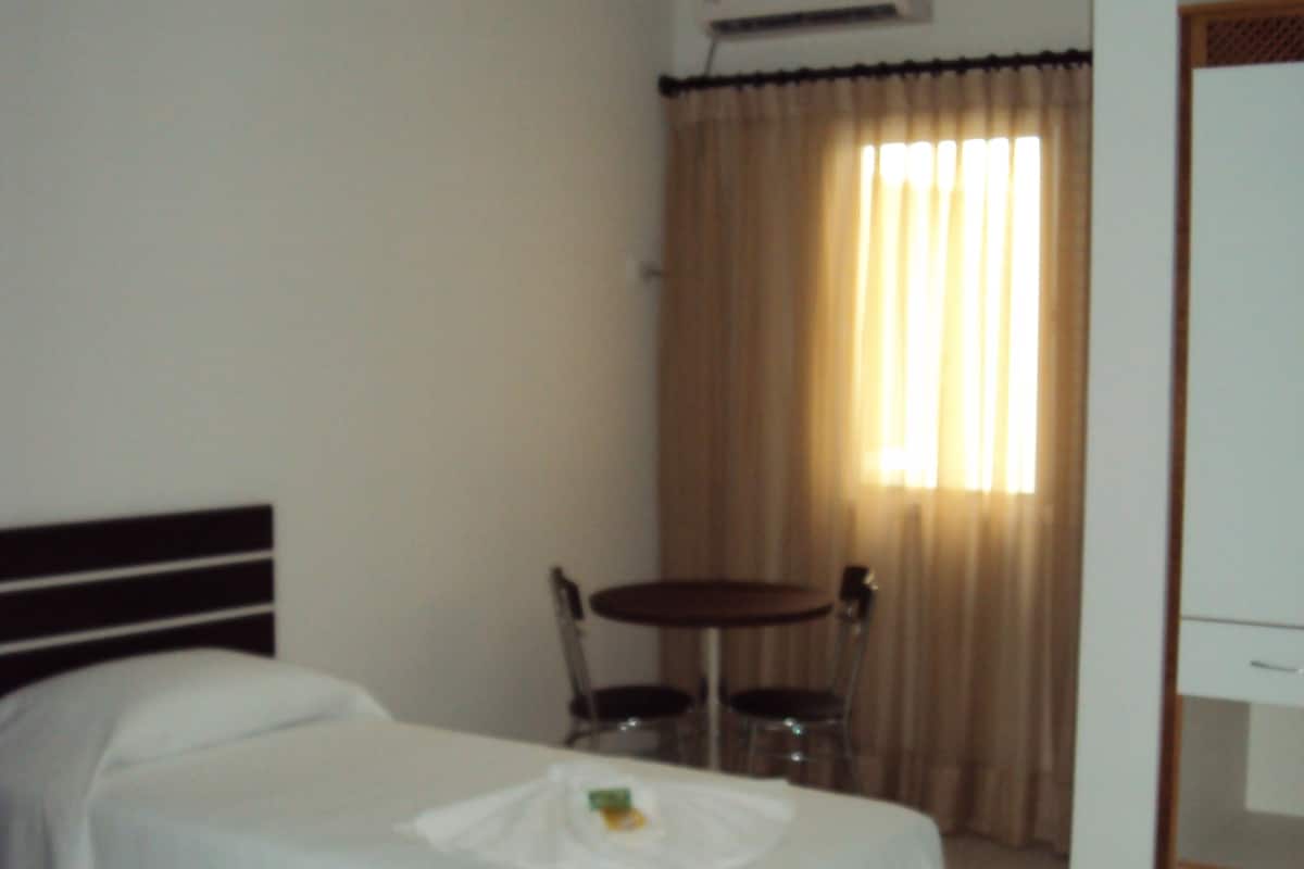 Habitación de hotel con dos camas, una mesita con bandeja, una silla, una mesa redonda y una ventana con cortinas.